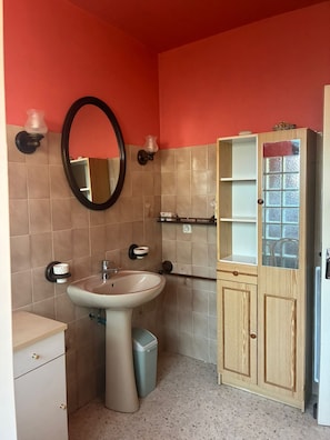 Une salle de bain avec un lavabo sur colonne, un miroir, un meuble avec des portes en verre et un porte-serviettes.