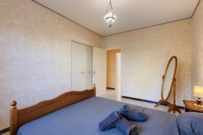 A bedroom with a large bed, a wooden headboard, a mirror, and a bedside table with a lamp.