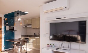 Una cocina moderna con microondas, estufa y horno integrados. Hay una zona de comedor con mesa y sillas, y un televisor de pantalla plana grande montado en la pared.