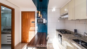 A modern kitchen with a dark wooden table, a built-in microwave, and a gas stove. - Studio in a Cond. With Pool, Setor Bueno - Txp1803 (Goiânia)