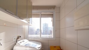 A small, modern bathroom with a window, a washing machine, and a yellow box. - Studio in a Cond. With Pool, Setor Bueno - Txp1803 (Goiânia)