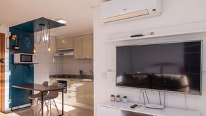 A modern kitchen with a built-in microwave, stove, and oven. There is a dining area with a table and chairs. A large flat-screen TV is mounted on the wall. - Studio in a Cond. With Pool, Setor Bueno - Txp1803 (Goiânia)