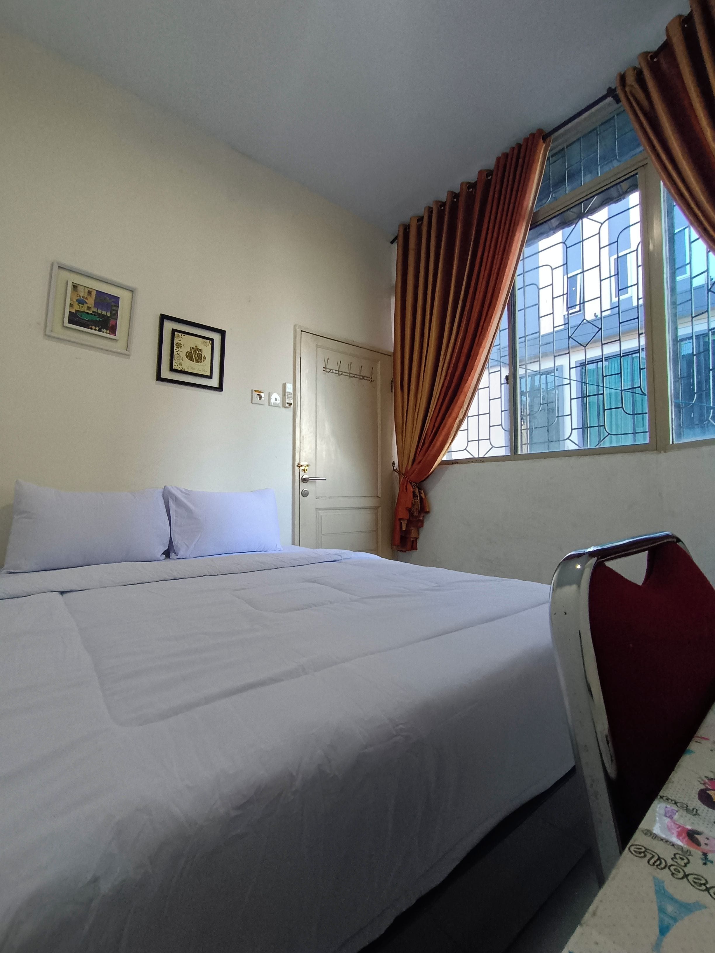 Una habitación con una cama, una ventana con cortinas, una puerta y dos cuadros en la pared.