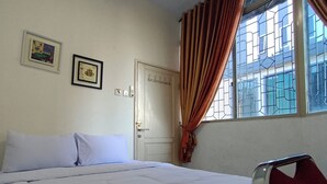 Una habitación con una cama, una ventana con cortinas, una puerta y dos cuadros en la pared.