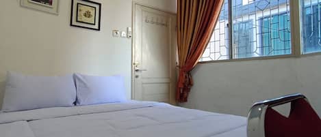 A room with a bed, a window with curtains, a door, and two framed pictures on the wall.