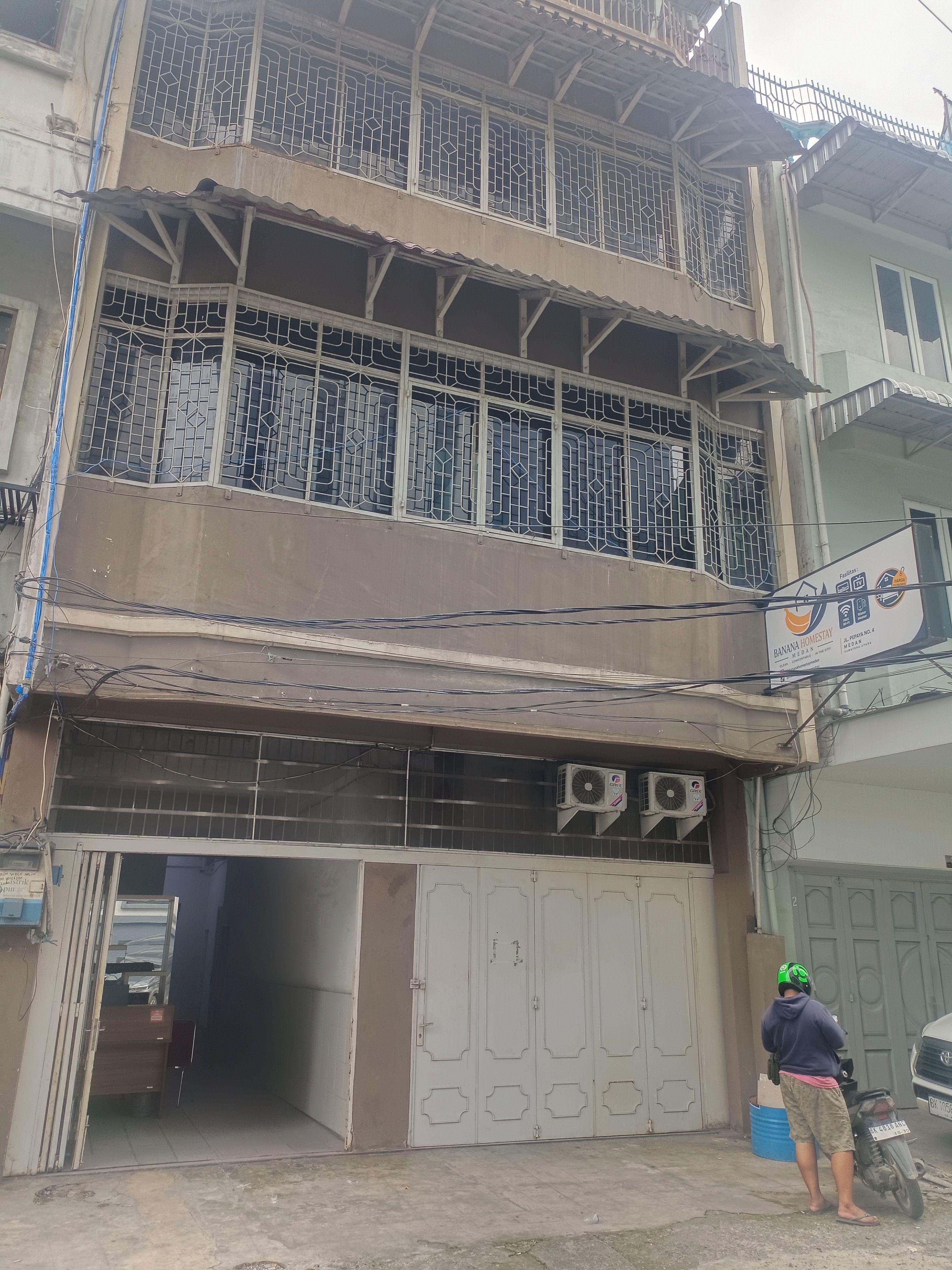 Un edificio de dos pisos con entrada protegida por una reja y un equipo de aire acondicionado en la pared.