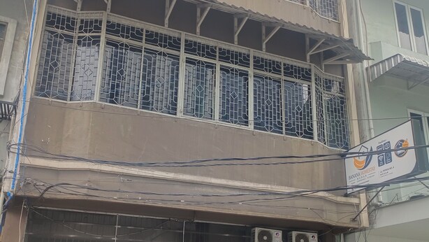 Un edificio de dos pisos con entrada protegida por una reja y un equipo de aire acondicionado en la pared.