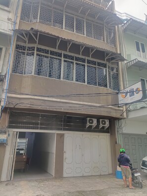 Un edificio de dos pisos con entrada protegida por una reja y un equipo de aire acondicionado en la pared.
