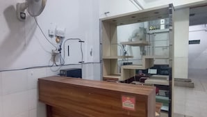 Un mostrador de recepción con acabado de madera, un ventilador de pared y una puerta entreabierta que da a una habitación con estanterías y equipos.