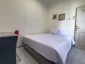 A simple room with a bed, a desk, and a door. - Banana Homestay Medan (Medan)