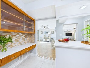 Een moderne keuken met een houten kast, een kookeiland met glazen deuren en een eethoek met televisie en plafondventilator.