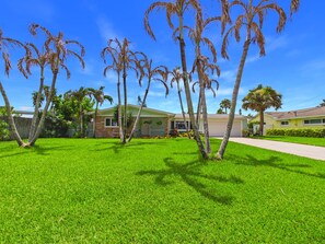 A residential area with a well-maintained lawn, palm trees, and houses with a light green exterior. - Whether you're bringing your boat, planning a family vacation, or simply looking for a peaceful coastal retreat, this home delivers an unforgettable Space Coast experience. (Cocoa Beach)