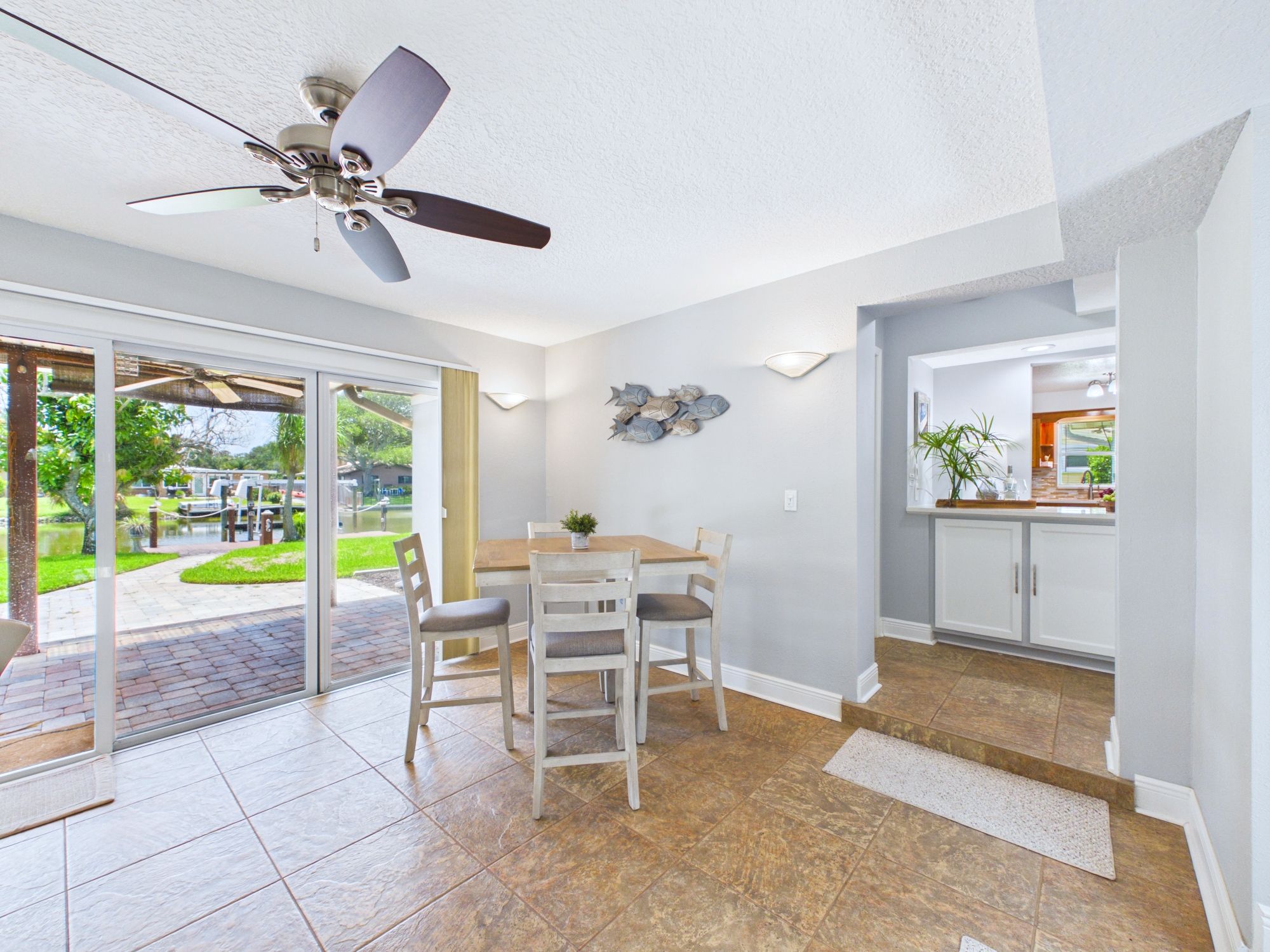 Un coin repas avec une table et des chaises, un ventilateur de plafond et une vue sur une terrasse extérieure, accessible par des portes vitrées.