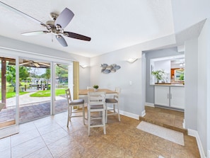 A dining area with a table and chairs, a ceiling fan, and a view through glass doors to an outdoor patio. - Whether you're bringing your boat, planning a family vacation, or simply looking for a peaceful coastal retreat, this home delivers an unforgettable Space Coast experience. (Cocoa Beach)