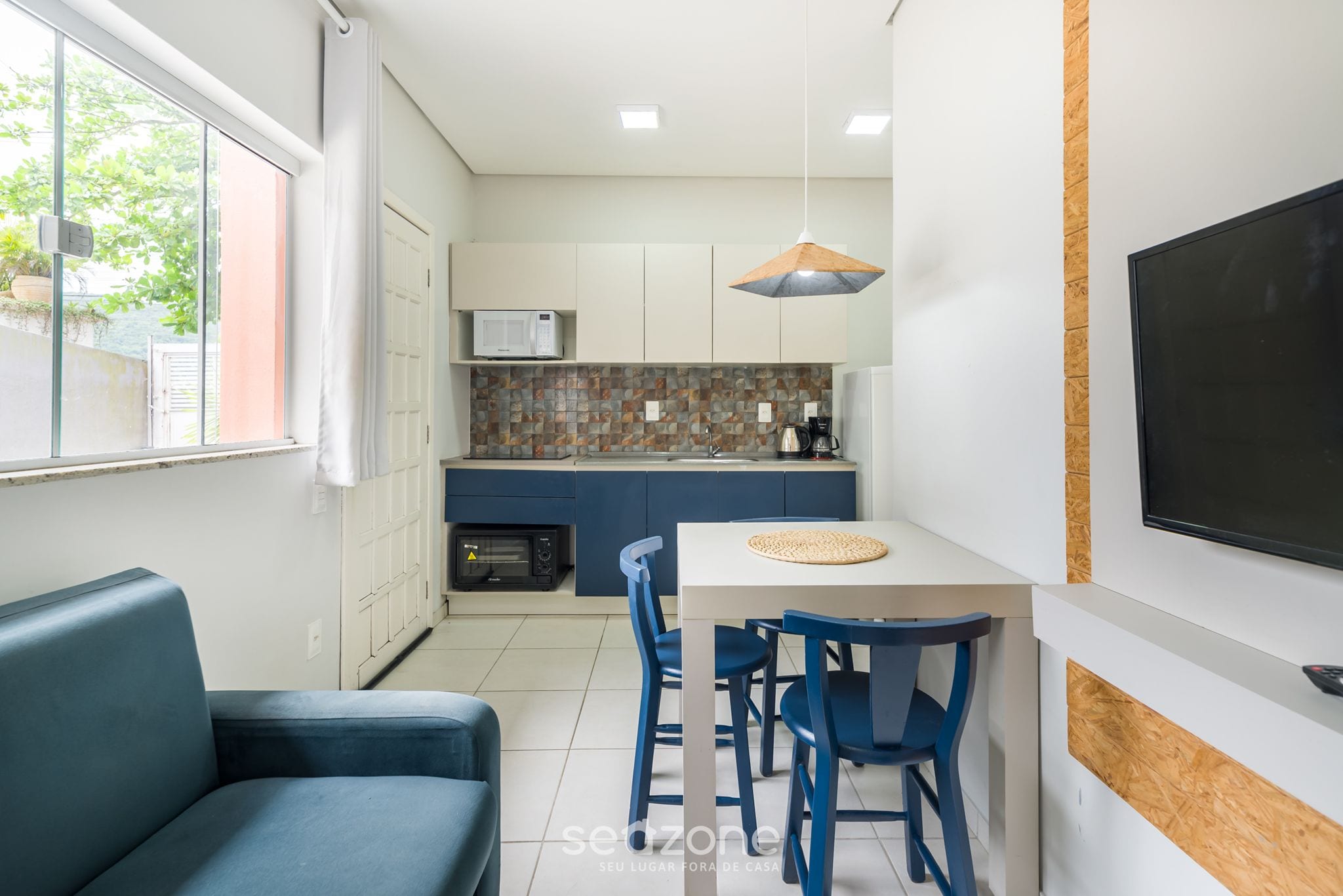 A compact kitchen with a microwave, coffee maker, and a small oven. There is a dining area with a table and chairs, and a TV mounted on the wall.