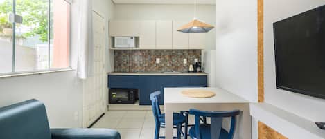 Cocina compacta con microondas, cafetera y horno pequeño. Cuenta con un comedor con mesa y sillas, y un televisor montado en la pared.