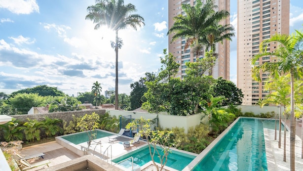 A rooftop swimming pool with lounge chairs, surrounded by greenery and tall buildings. - Ap w/ Amazing View and Pool the Building - Txp1101 (Goiânia)