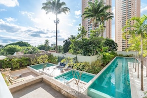 Una piscina al terrat amb gandules, envoltada de vegetació i edificis alts.