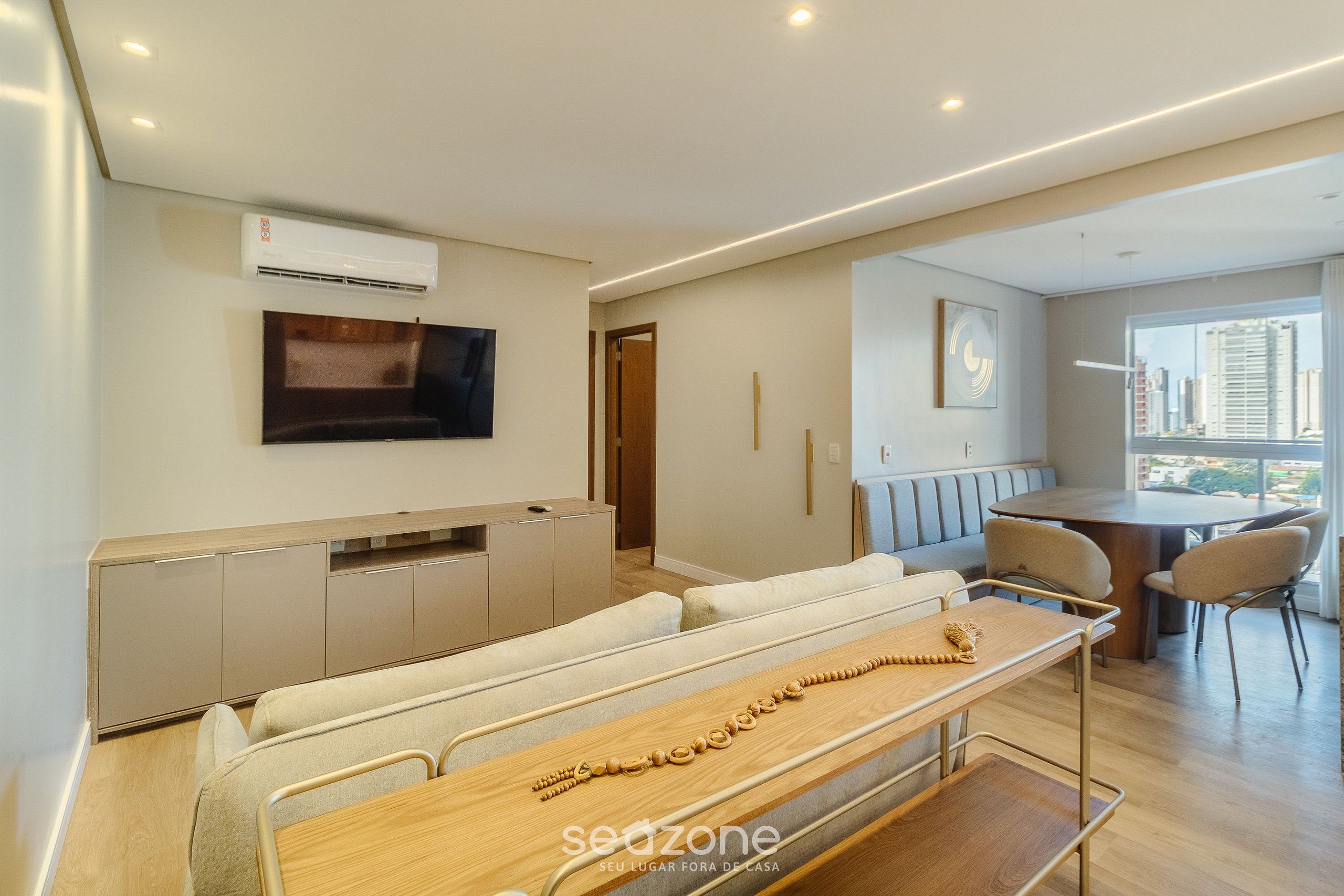 A modern living room with a sofa, a wooden table, and a TV mounted on the wall.