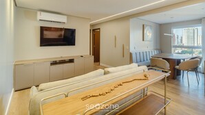 A modern living room with a sofa, a wooden table, and a TV mounted on the wall. - Ap w/ Amazing View and Pool the Building - Txp1101 (Goiânia)