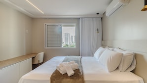 A hotel room with a bed, a desk, a chair, a window with curtains, and an air conditioning unit. - Ap w/ Amazing View and Pool the Building - Txp1101 (Goiânia)