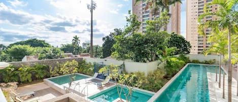 A rooftop swimming pool with lounge chairs, surrounded by greenery and tall buildings.