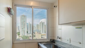 A modern kitchen with a large window, a built-in sink, and a view of high-rise buildings. - Ap w/ Amazing View and Pool the Building - Txp1101 (Goiânia)