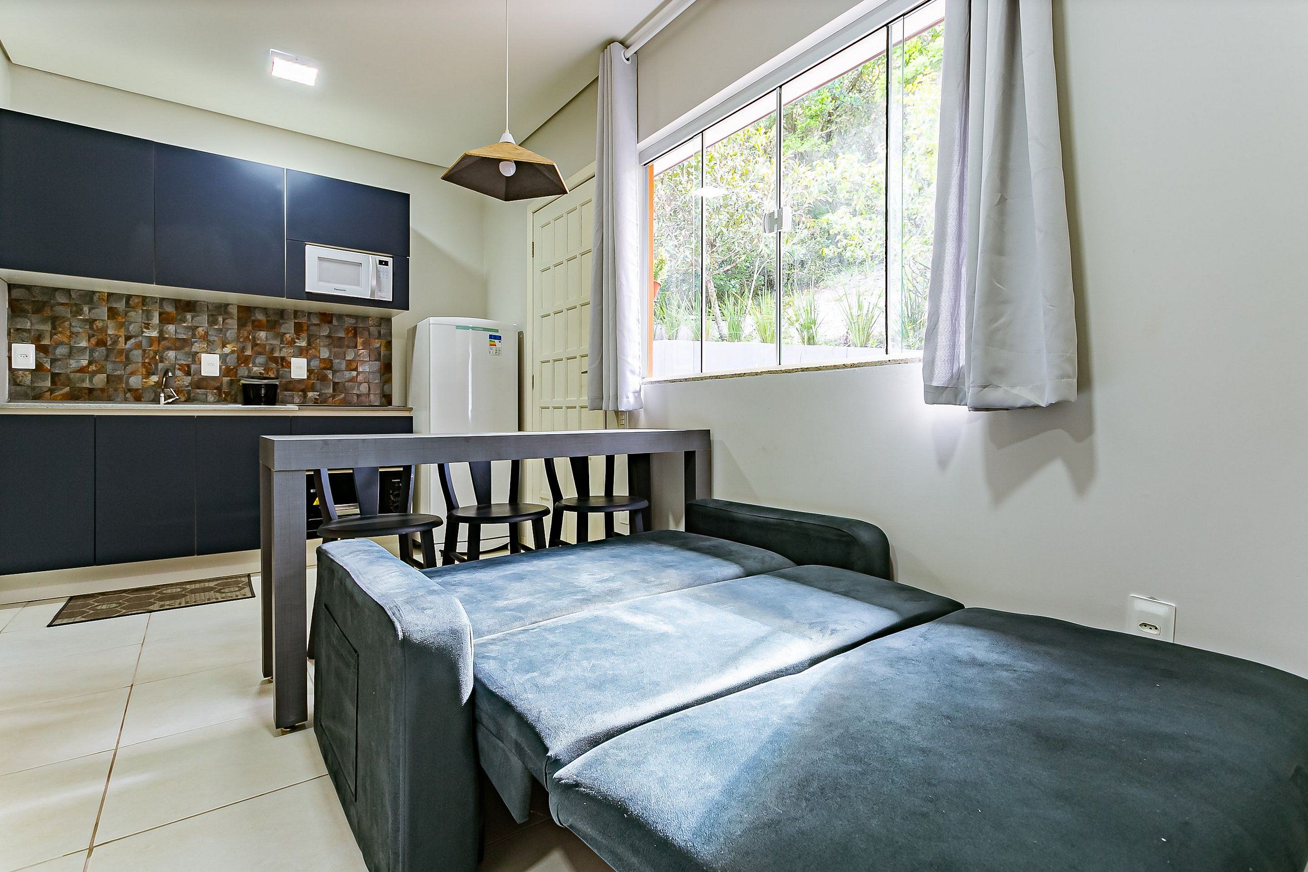 A small, modern room with a bed, a kitchenette, and a window with curtains.
