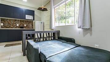 A small, modern room with a bed, a kitchenette, and a window with curtains.