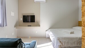 A hotel room with a bed, a TV mounted on the wall, a sofa, and a wooden accent wall. - Comfortable Studio Facing the Lagoon Sdr008 (Florianópolis)