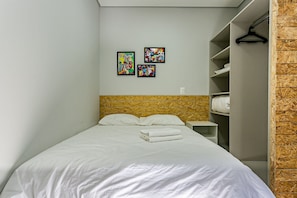 Un lit bien fait, avec du linge de lit blanc, une tête de lit en bois et un mur orné de trois œuvres d’art colorées.
