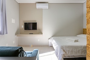 Una habitación de hotel con cama, televisor montado en la pared, escritorio con silla y ventana.