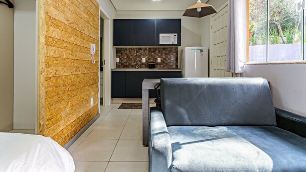 A compact living space with a kitchenette, a sofa, and a window with a view of greenery. - Comfortable Studio Facing the Lagoon Sdr008 (Florianópolis)