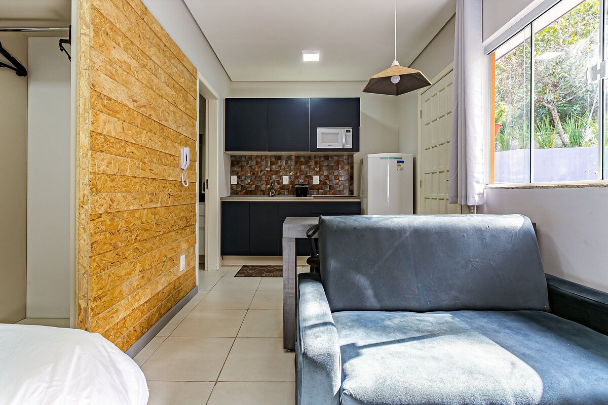 Un espace de vie compact comprenant un coin cuisine, un canapé et une fenêtre donnant sur un paysage verdoyant.