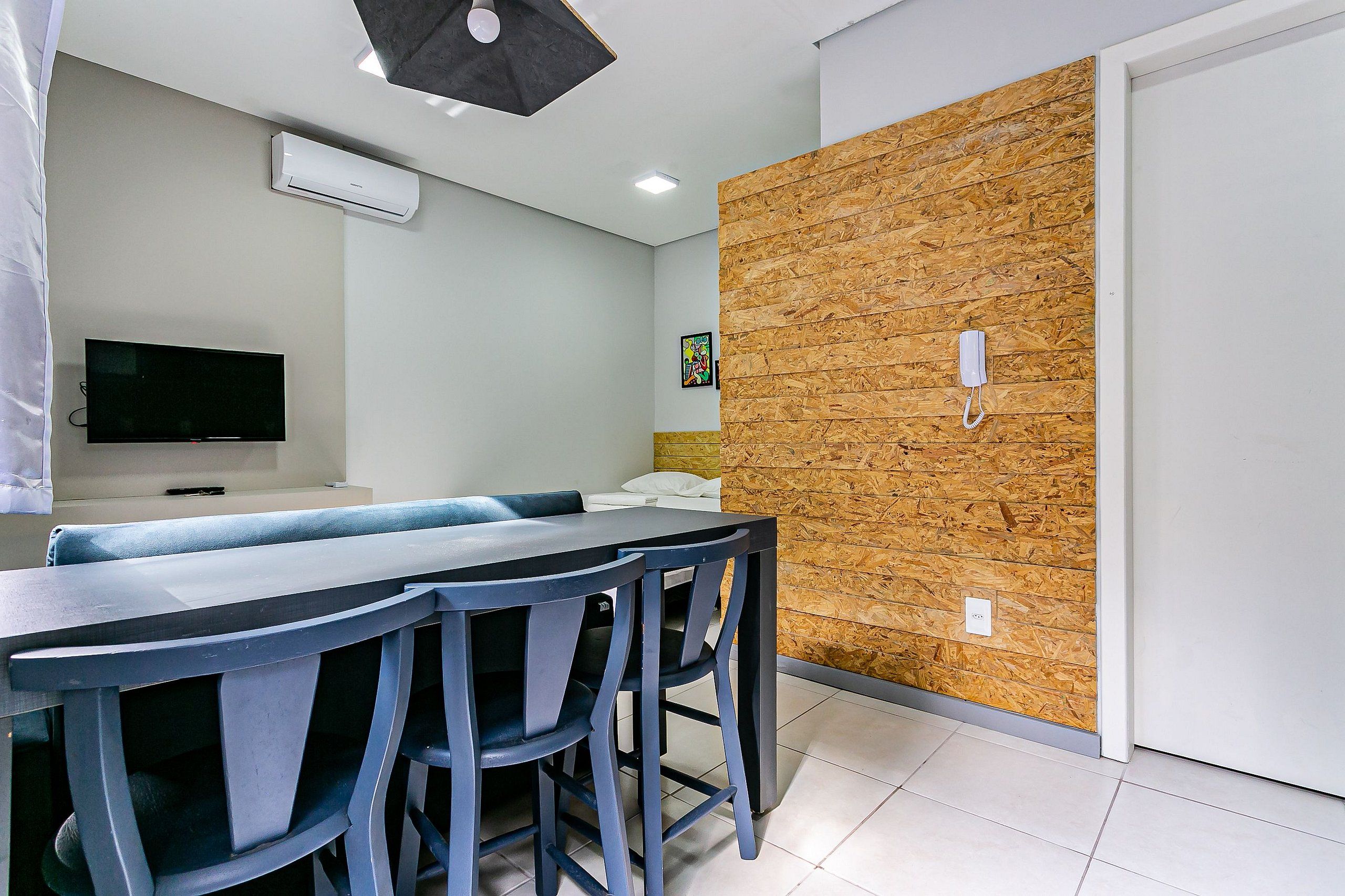 A modern dining area with a long table and chairs, a flat-screen TV, and a wooden accent wall.