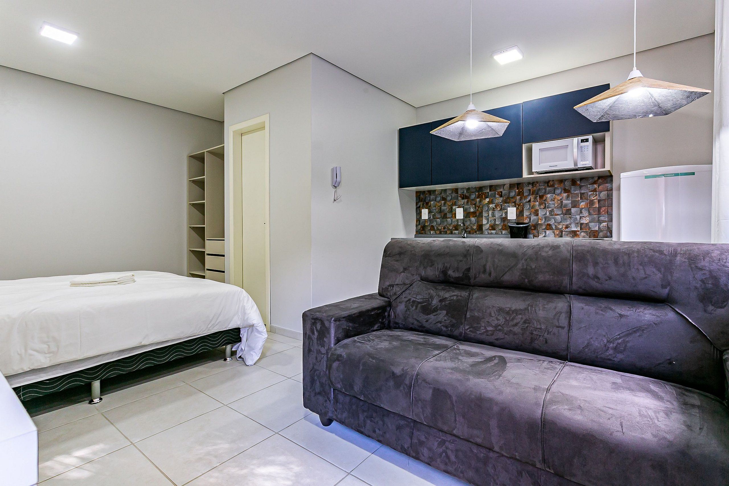 A modern room with a bed, a sofa, a kitchen area with a microwave, and a water dispenser.