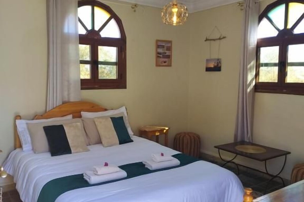 A bedroom with a bed, a table, and a hanging light fixture.