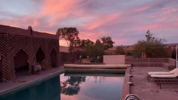 Una piscina con una estructura de ladrillo a un lado y sillas de descanso al otro.
