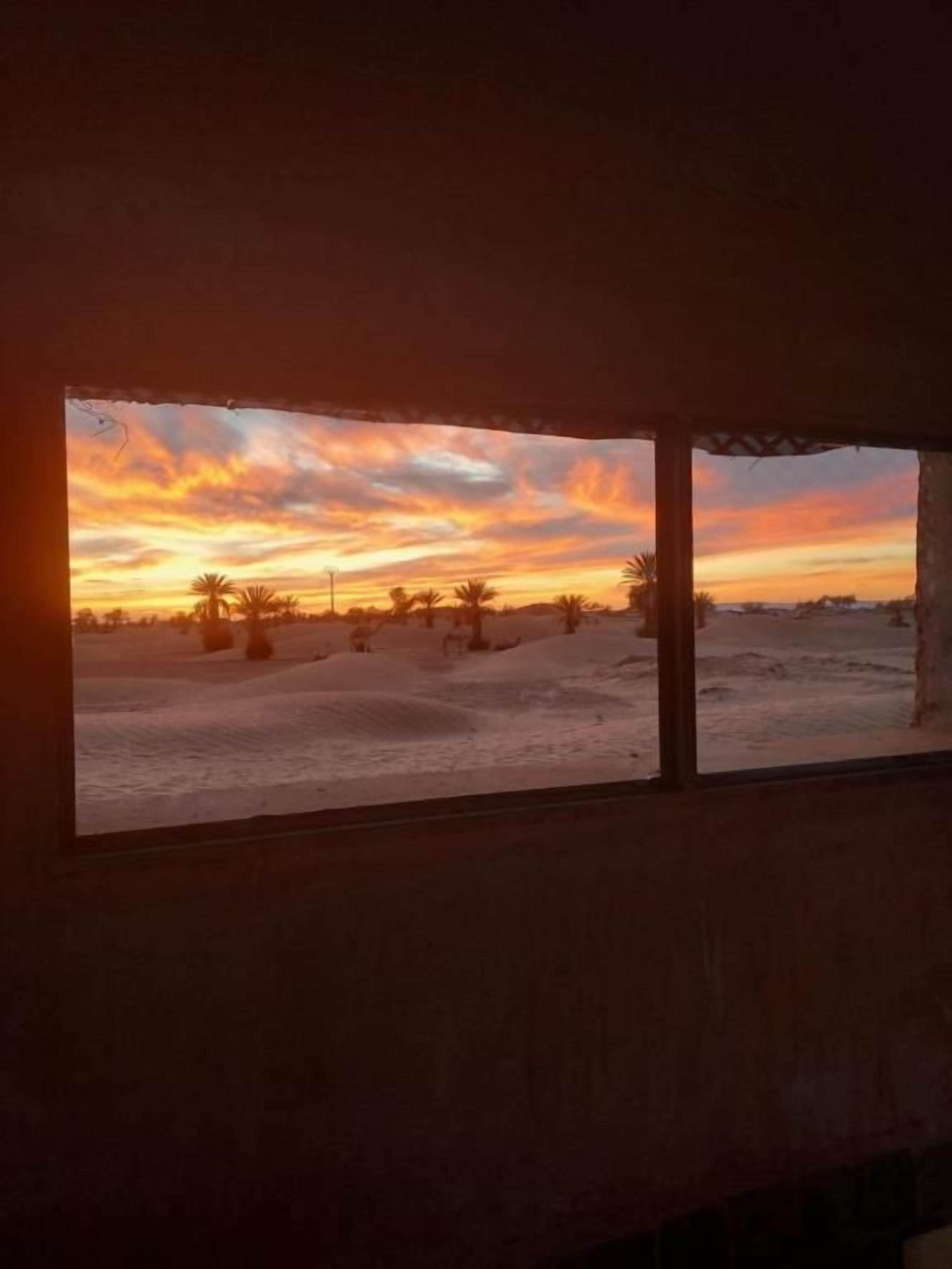 A room with a view of a sunset over a landscape with palm trees.