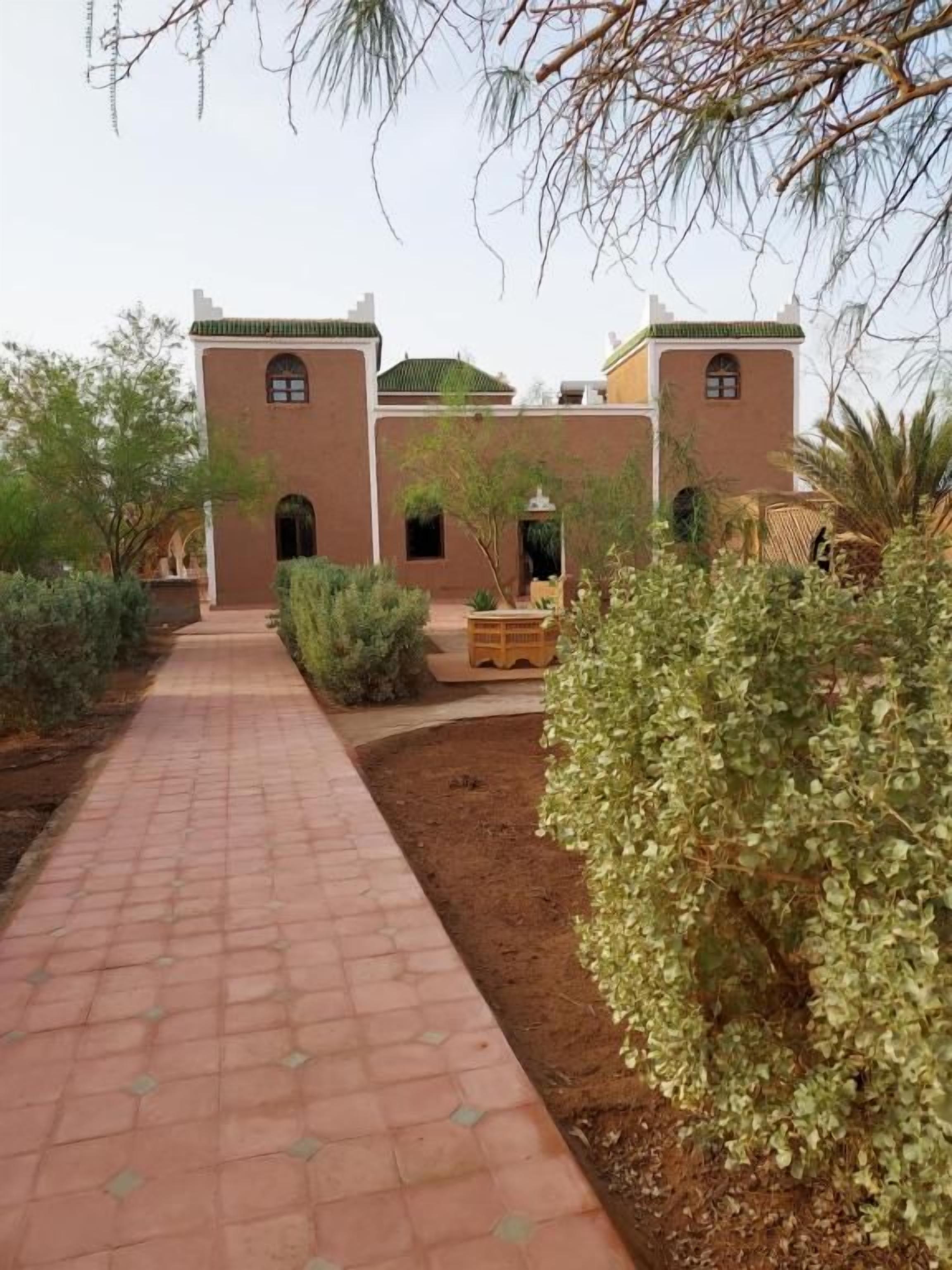 Un sendero conduce a un edificio de estilo arquitectónico tradicional, rodeado de vegetación y un cielo despejado.