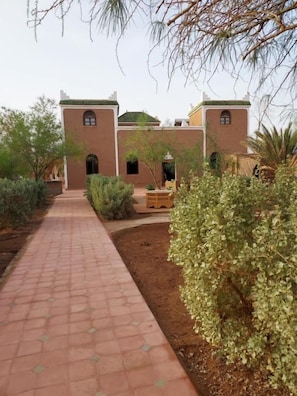 Un sendero conduce a un edificio de estilo arquitectónico tradicional, rodeado de vegetación y un cielo despejado.