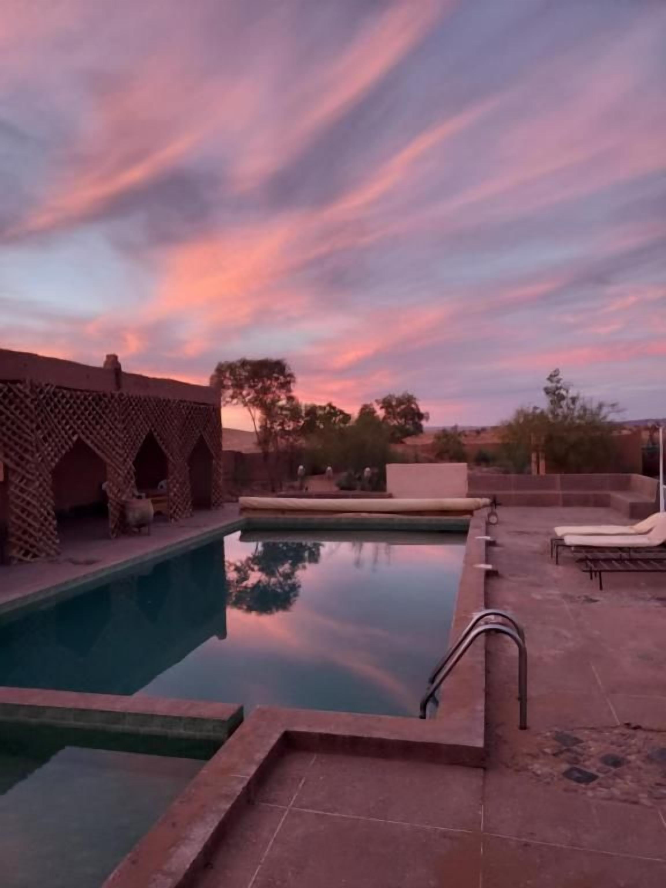 Una piscina con una estructura de ladrillo a un lado y sillas de descanso al otro.