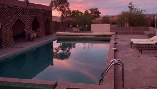 Una piscina con una estructura de ladrillo a un lado y sillas de descanso al otro.