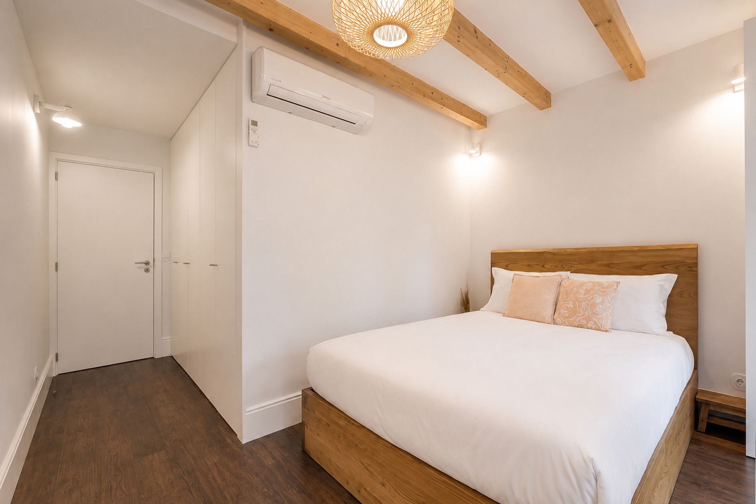 A bedroom with a wooden headboard, a white bedspread, and a wooden floor.