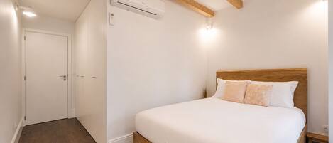 Une chambre à coucher avec une tête de lit en bois, un couvre-lit blanc et un plancher en bois.