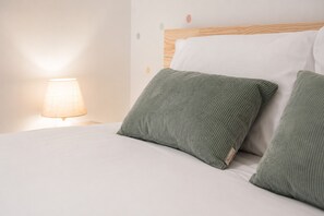 Ein Bett mit weißer Bettwäsche und zwei grünen Kissen, eine Lampe auf dem Nachttisch und ein hölzernes Kopfteil.