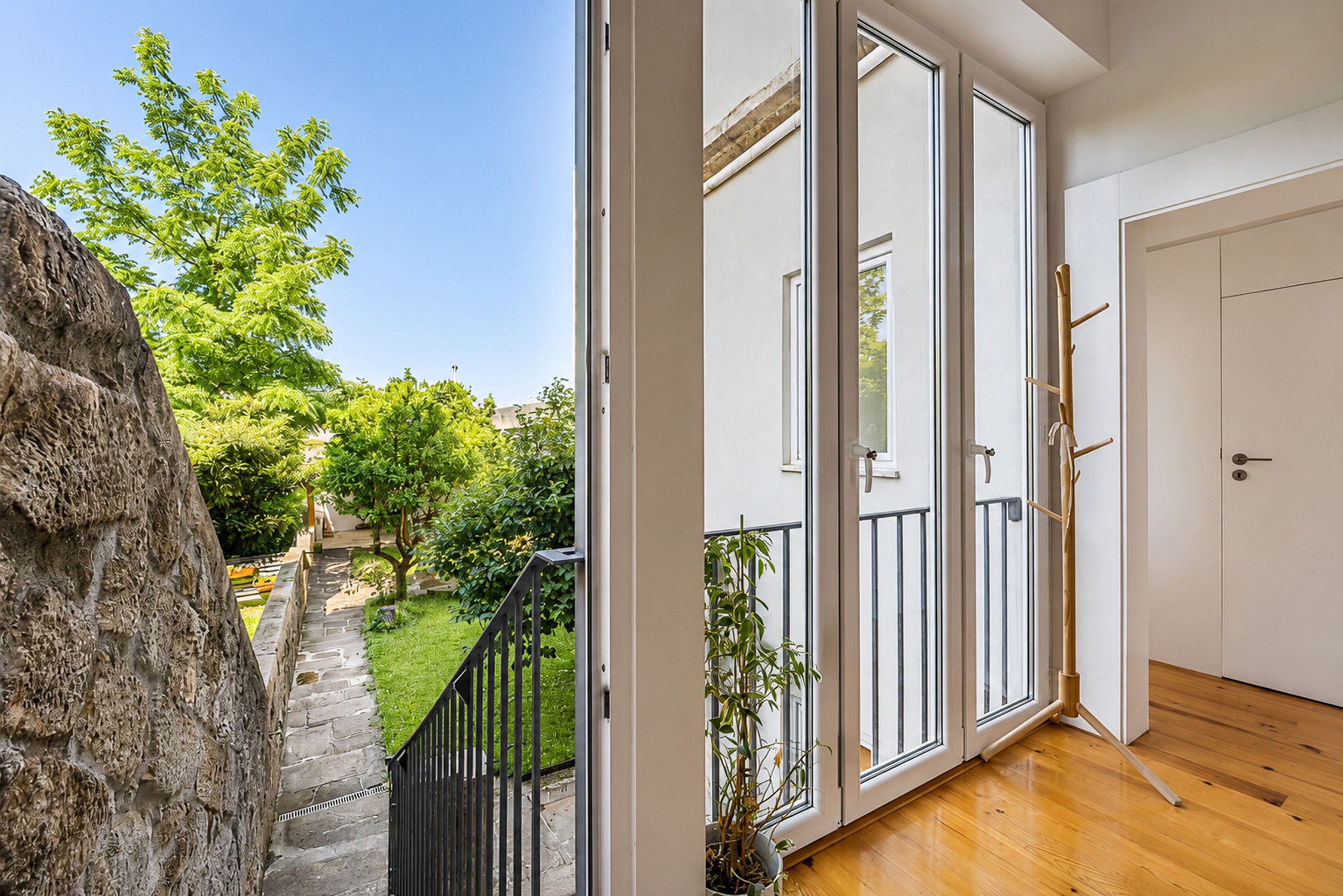 Une pièce dotée d’une grande porte-fenêtre coulissante donnant sur un jardin, d’un plancher en bois et d’une porte blanche.