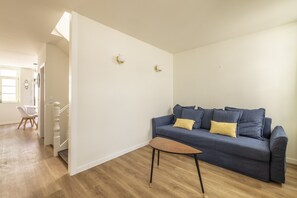 Una sala de estar moderna con un sofá azul, una mesita de madera y una pared blanca con dos apliques.