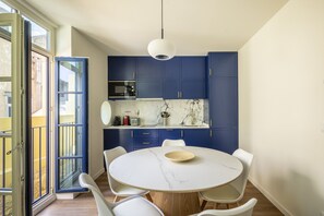 A modern kitchen with blue cabinets, a white marble countertop, and a round dining table with chairs. - Taipas House in Porto 2 (Porto)