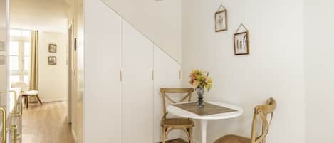 Una habitación con una mesa blanca, dos sillas, un florero con flores y una escalera que lleva a otra habitación.